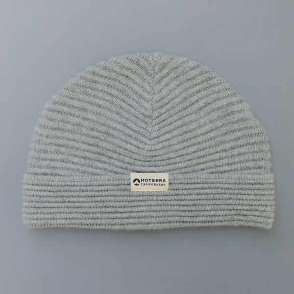 A ribbed grey beanie with a white woven patch with the Moterra Campervans logo stitched onto it.