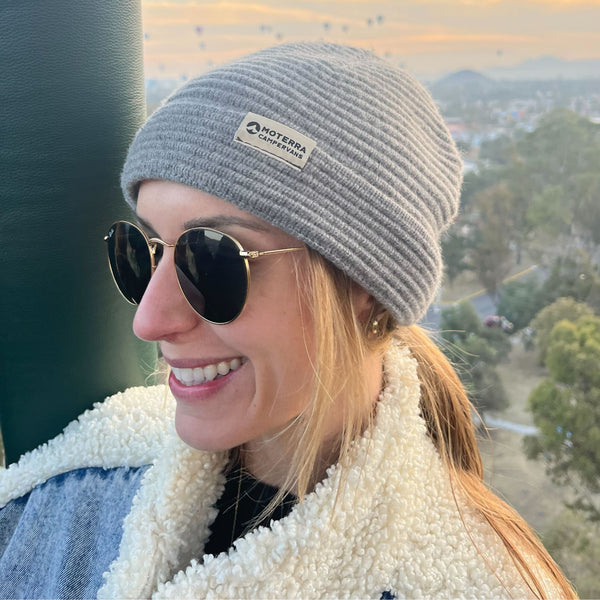 Smiling woman wearing a gray ribbed beanie with a Moterra Campervans logo patch.